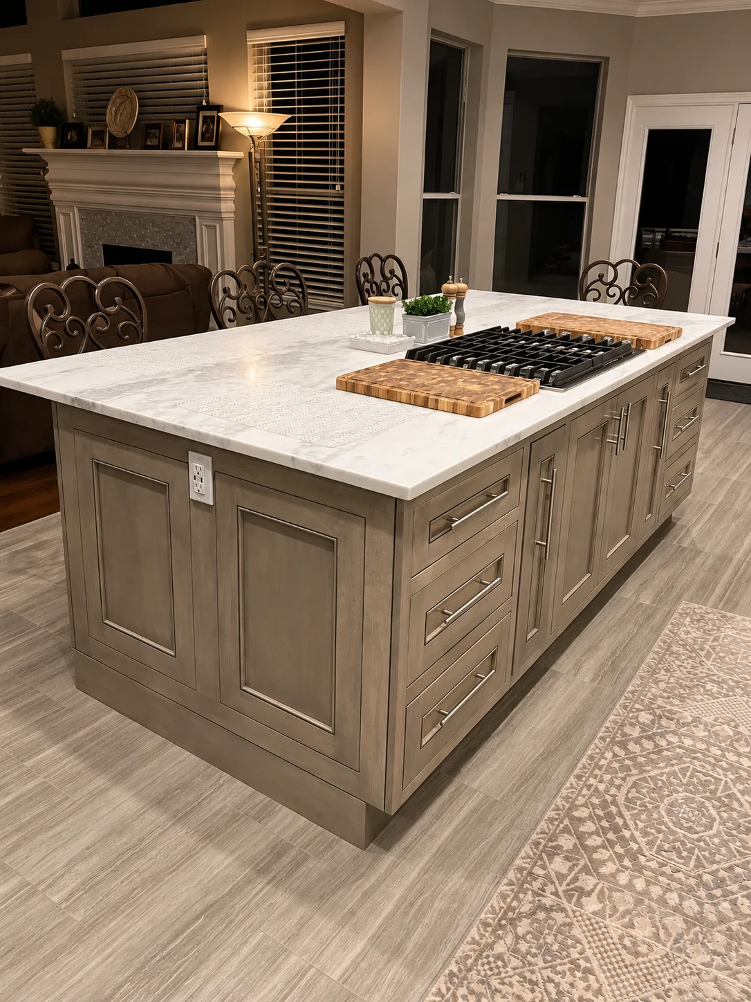 Gray paneled kitchen island with gas cooktop, wood cutting boards, and evening living room beyond